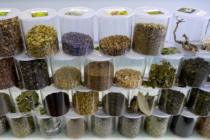 Čtyři řady malých průhledných plastových nádob jsou naskládané na sobě. Každá z nich obsahuje určité množství mletých bylinek v různých tlumených barvách. 